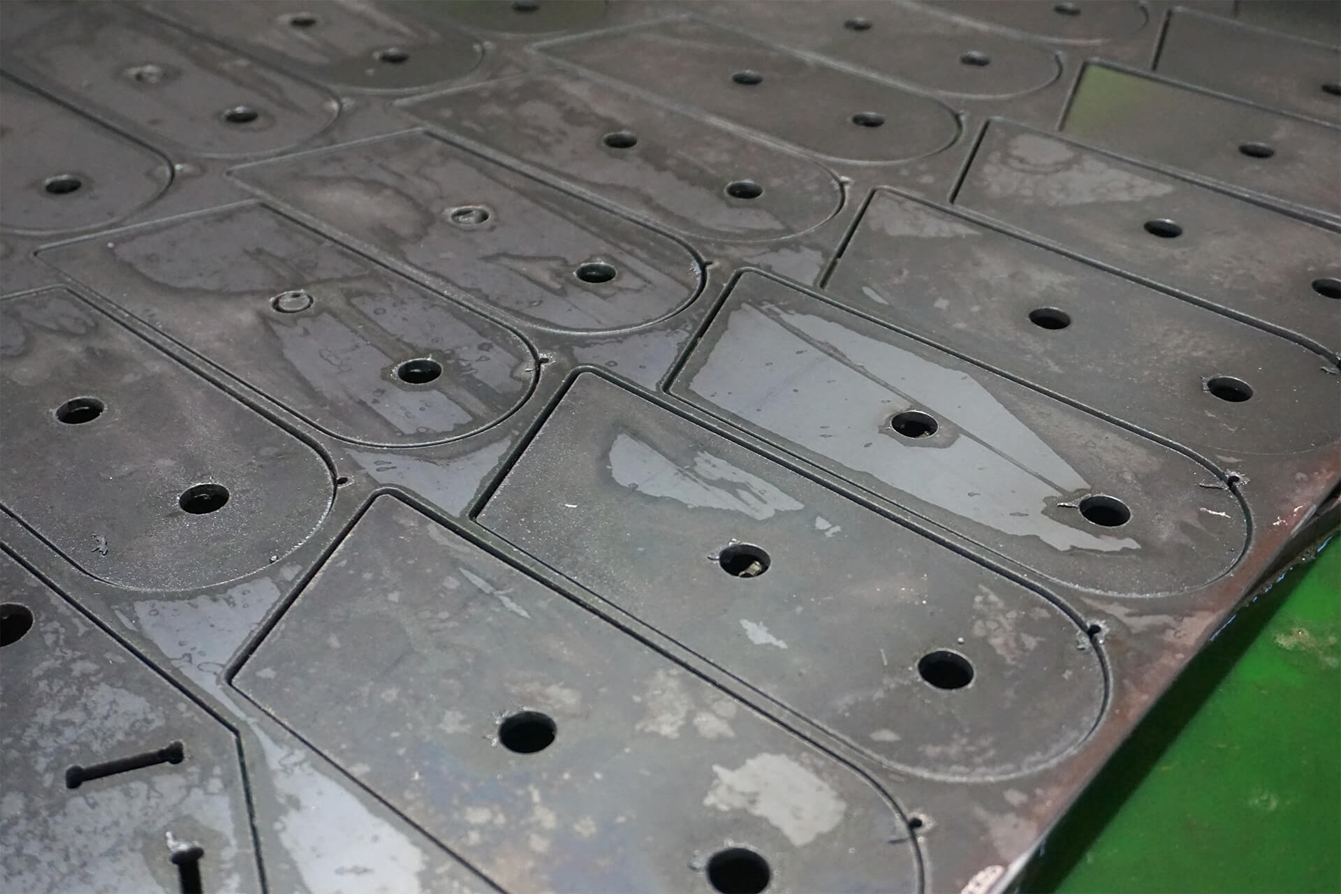 An array of smilar steel parts that are cut and still sitting on the plasma table.